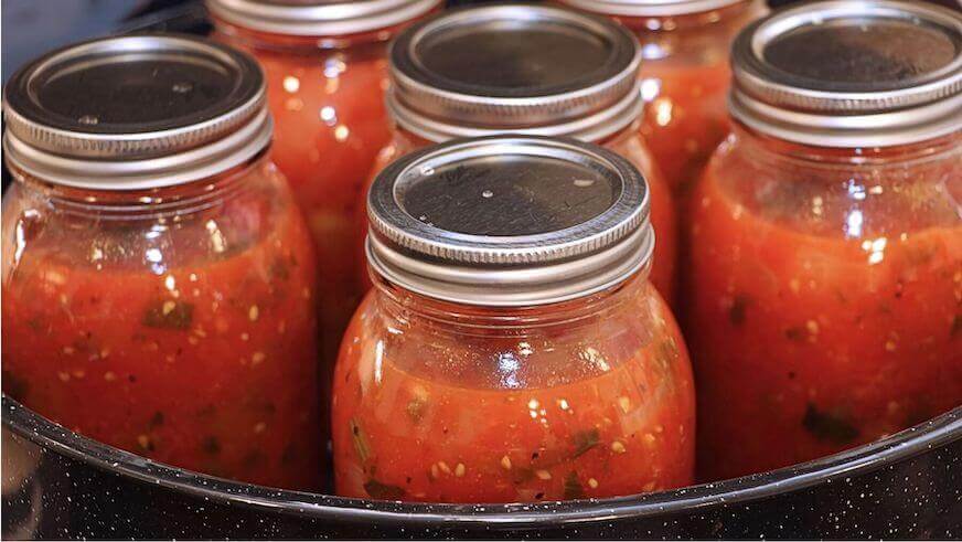 A handful of glass jars filled with salsa or gazpacho sit in a large black kettle.