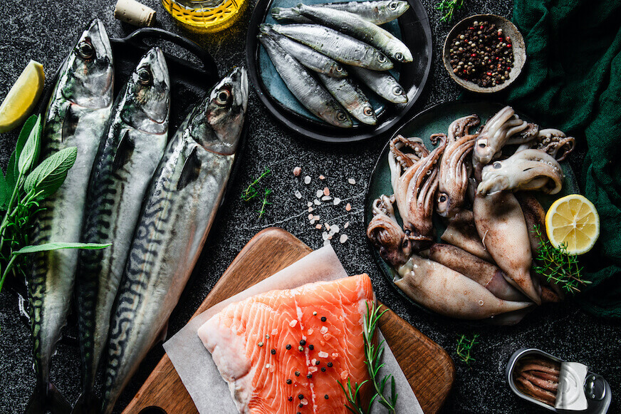 Overhead view of different types of fish on dark plates and cast iron skillets.