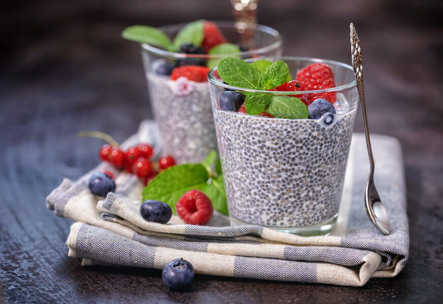 Two short glasses with chia seed pudding, topped with fresh berries and a sprig of mint.