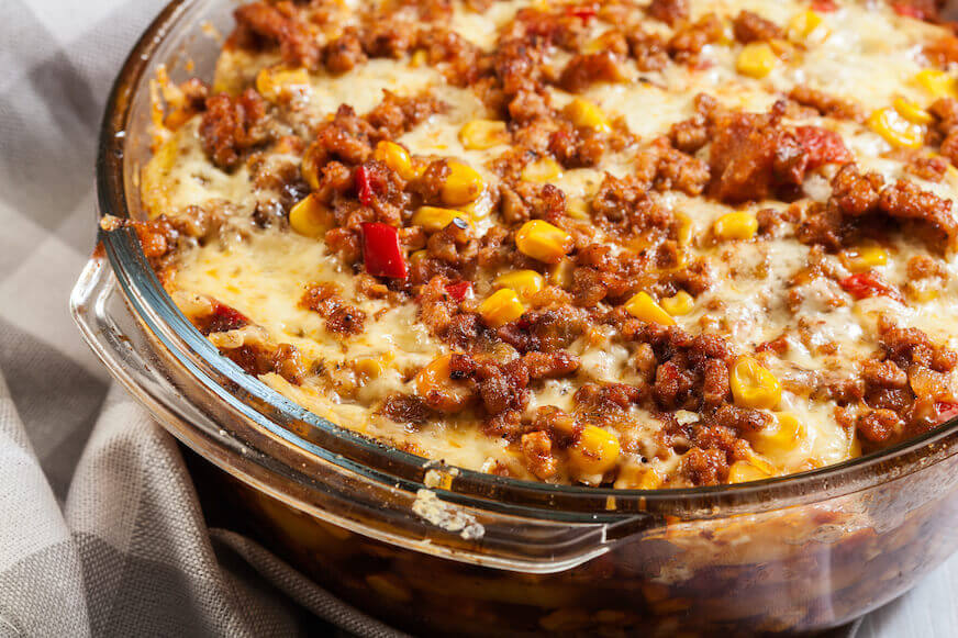 A closeup of a Mexican potato casserole with minced meat in an oval glass baking dish.