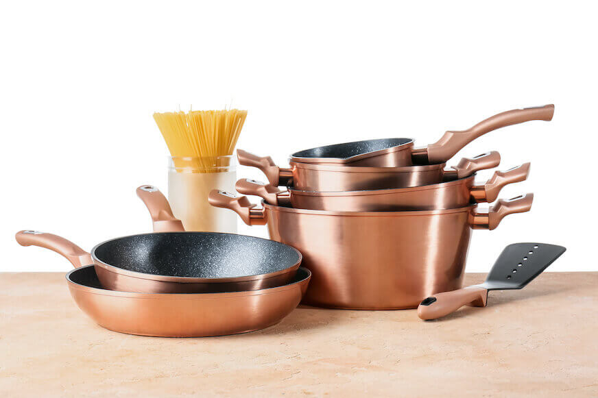 A set of copper kitchen utensils and jar with raw spaghetti on table against white background