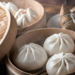 Three steamed bao buns sit in a small wooden basket.