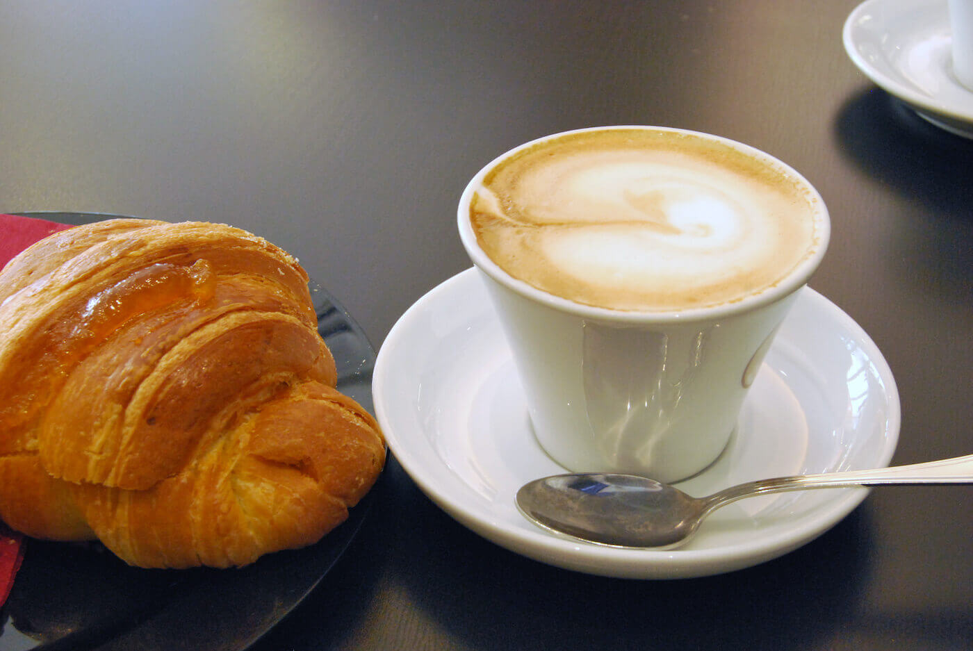 A cornetto sits next to a small cup of cappuccino