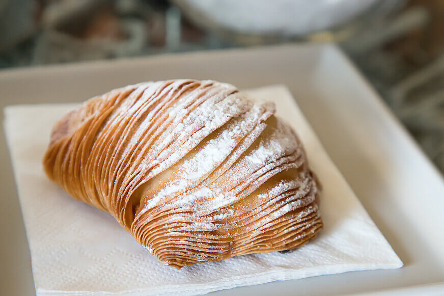 Sfogliatella diletakkan di atas piring putih dan ditaburi gula manisan.