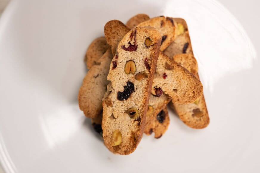 Pemandangan dari atas potongan biscotti almond yang ditumpuk di piring putih.