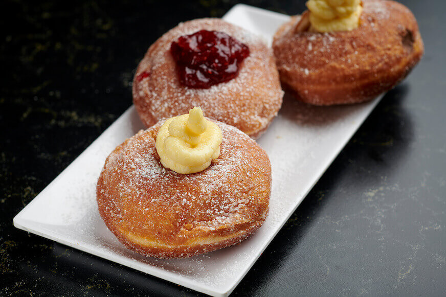 Tiga bomboloni Italia dengan krim dan selai jeruk di piring putih.